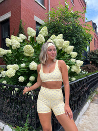 girl standing in athletic yellow outfit with lavender headband leaned against iron fence with brick building background 