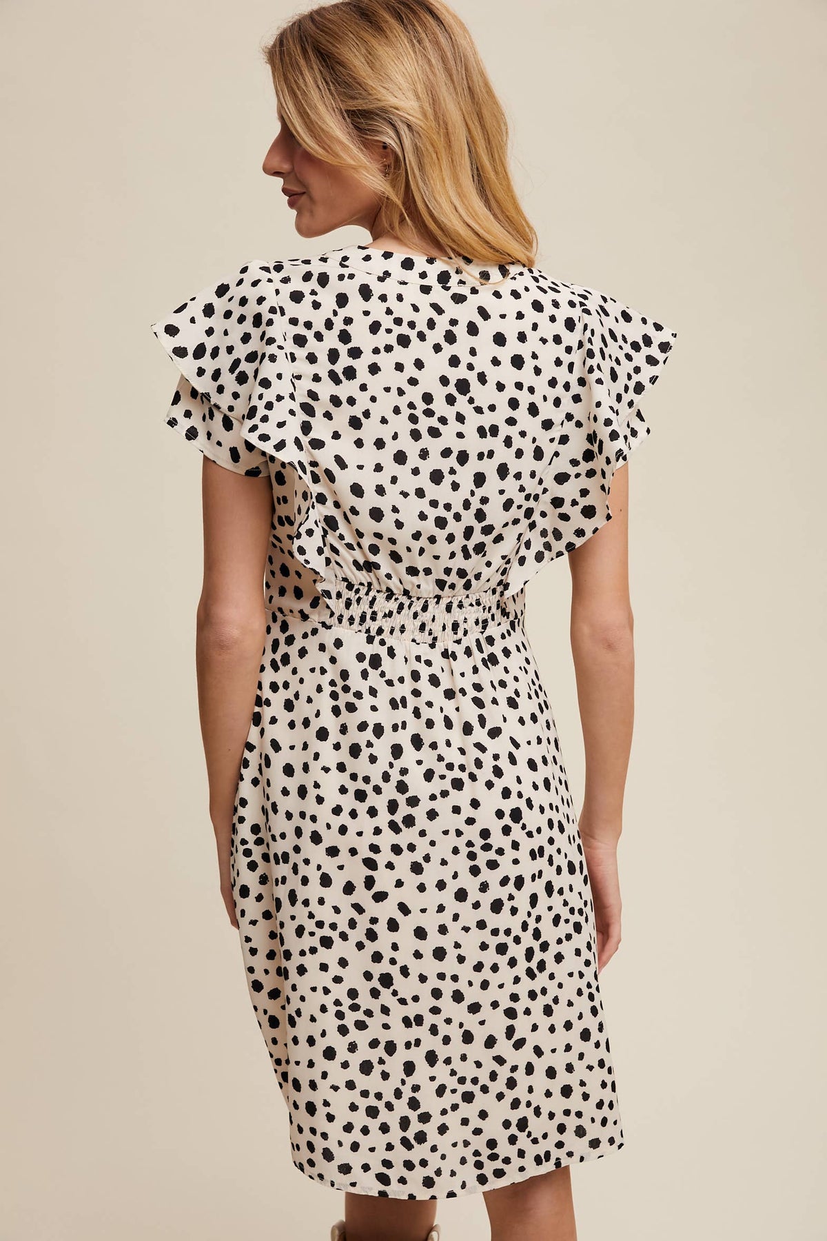 Back view of model wearing ruffled animal polka dot dress with flutter sleeves and gathered waist