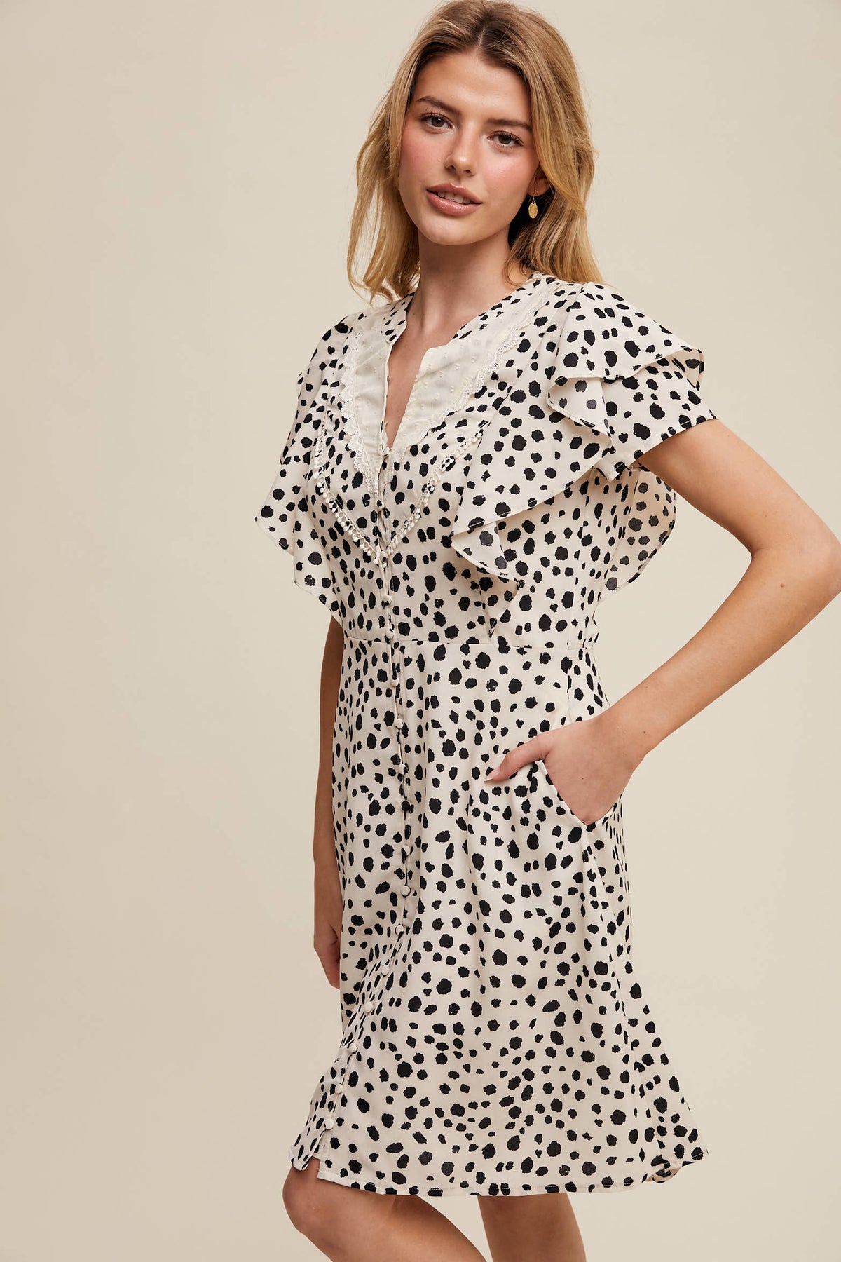 Side view of model wearing button-up animal print dress with ruffled neckline and hand in side pocket