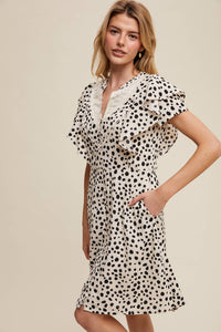 Side view of model wearing button-up animal print dress with ruffled neckline and hand in side pocket