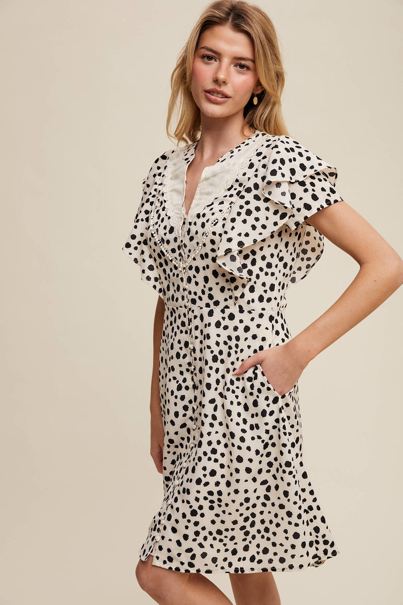 Side view of model wearing button-up animal print dress with ruffled neckline and hand in side pocket