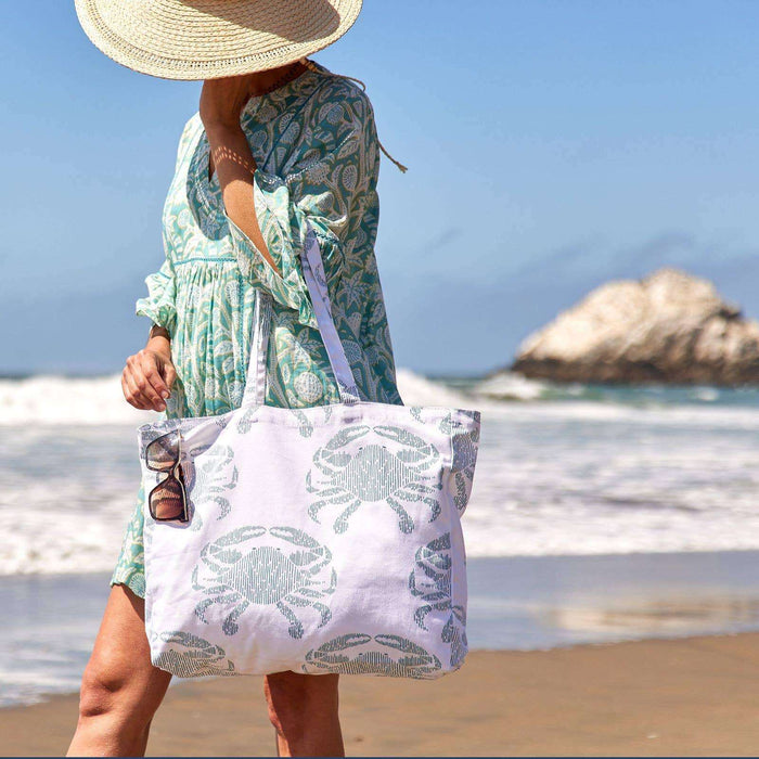 woman in beach dress and hat holding tote bag with crab print with beach background
